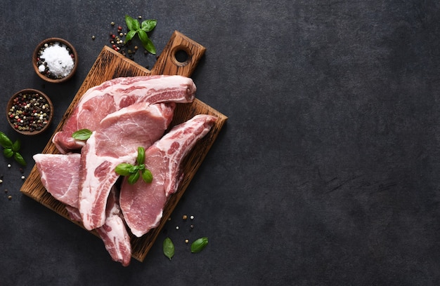 Raw pork steaks on a board with spices and basil on a dark background. Top view. Fresh meat. Ribs.