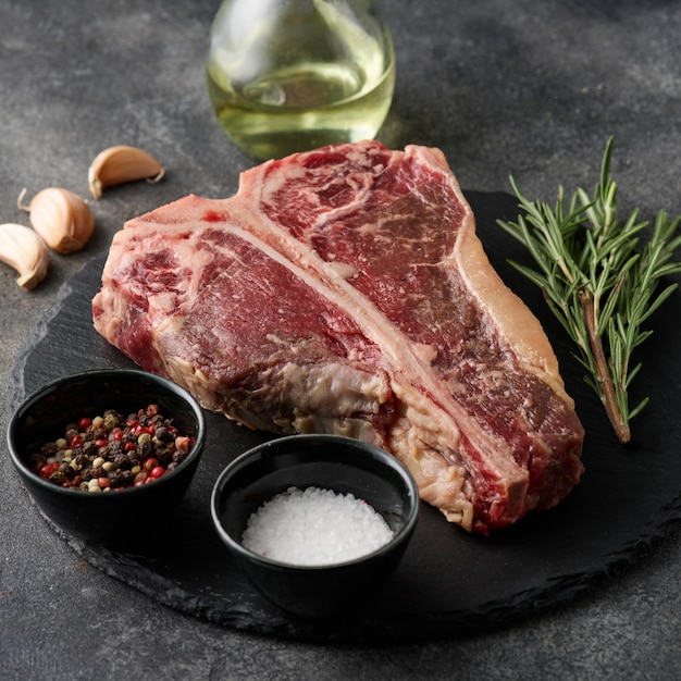 Raw porterhouse steak with spices lying on a dark grey table Raw fresh beef Tbone steak