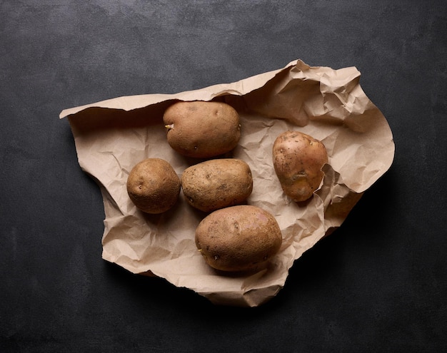 Raw potatoes lie on a brown piece of paper top view