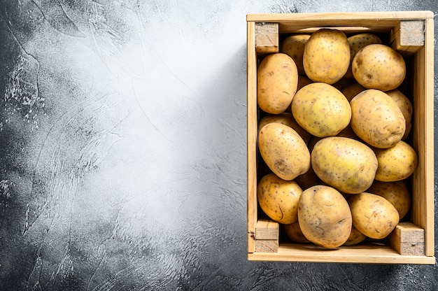 Raw Potatoes in an old wooden box on a table.  Gray background. Top view. Copy space