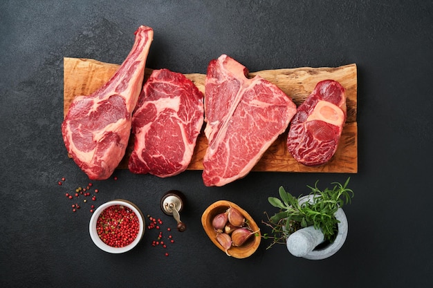 Raw prime steaks Variety of fresh black angus prime meat steaks Tbone New York Ribeye Striploin Tomahawk cutting board on black or dark background Set of various classic steaks Top view