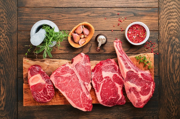 Raw prime steaks Variety of fresh black angus prime meat steaks Tbone New York Ribeye Striploin Tomahawk cutting board on black or dark background Set of various classic steaks Top view