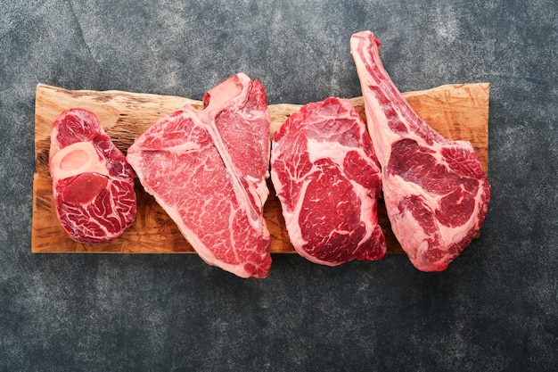 Raw prime steaks Variety of fresh black angus prime meat steaks Tbone New York Ribeye Striploin Tomahawk cutting board on black or dark background Set of various classic steaks Top view