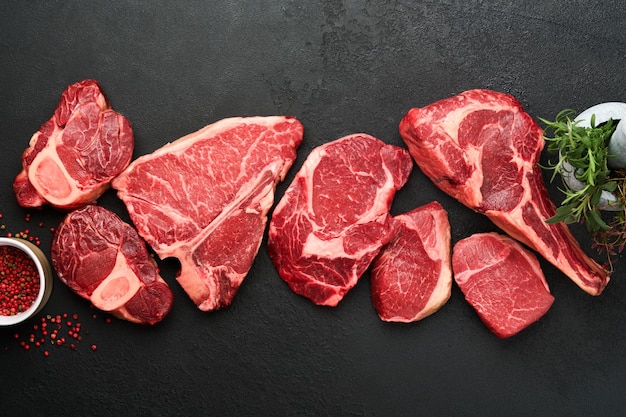 Raw prime steaks Variety of fresh black angus prime meat steaks Tbone New York Ribeye Striploin Tomahawk cutting board on black or dark background Set of various classic steaks Top view