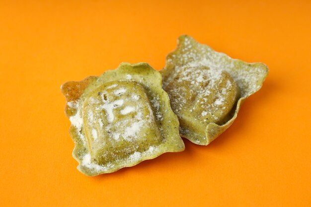 Raw ravioli with flour on orange background