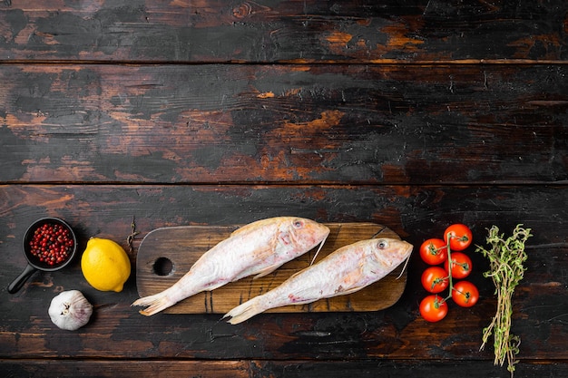 Raw red mullet or sultanka fresh whole fish with ingredients and herbs on old dark wooden table background top view flat lay with copy space for text