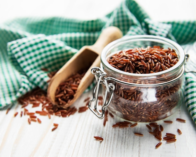 Raw red rice in glass jar on a white wooden surface