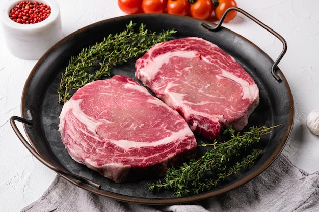 Raw rib eye beef steak with pepper and herbs set, on white stone table background