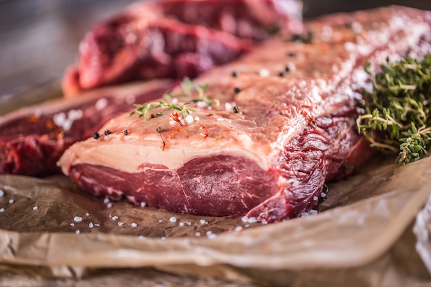 Raw rib eye beef steak with salt spices and herbs.