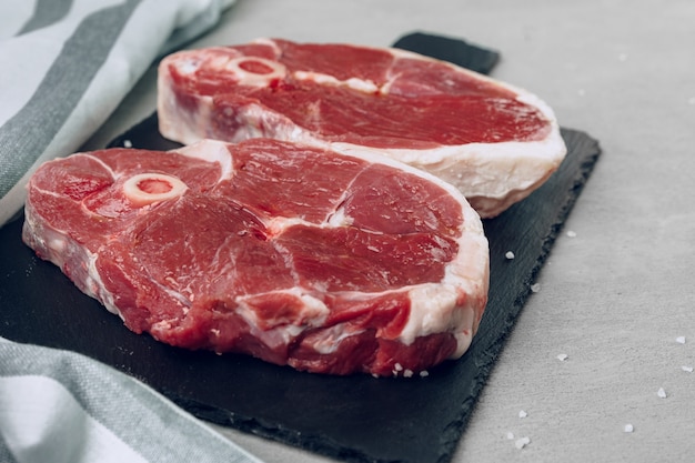 Raw rib-eye beef steak on wooden cutting board on gray