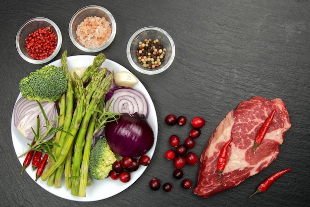 Raw rib eye steak with spices and vegetables