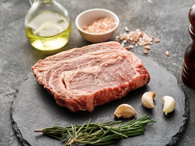 Raw ribeye steak on a black board with garlic and rosemary Fresh marbled beef