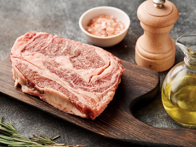 Raw ribeye steak on a wooden board Preparing raw beef steak for barbecue grill