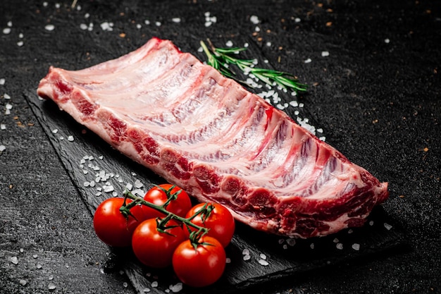 Raw ribs on a stone board with tomatoes and pieces of salt