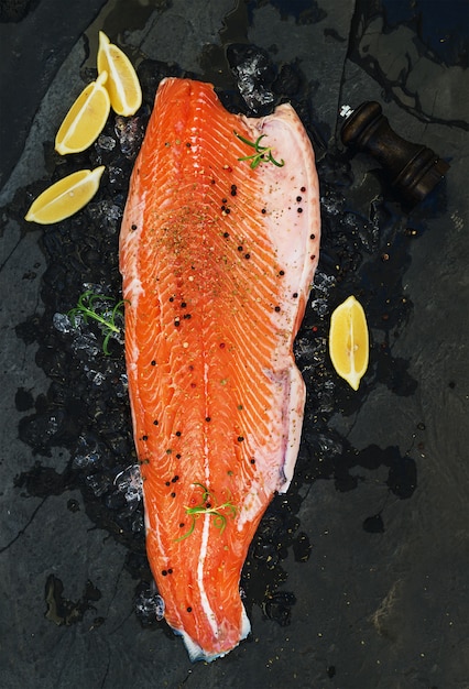 Raw salmon filet with lemon and rosemary on chipped ice over dark stone 