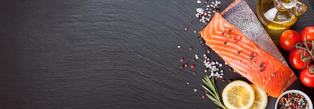 Raw salmon fillet and ingredients for cooking on black slate background