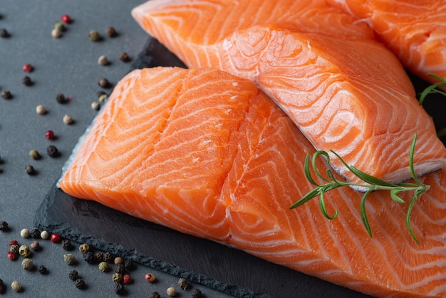 Raw salmon fillet and ingredients for cooking seasonings and herbs on a dark background