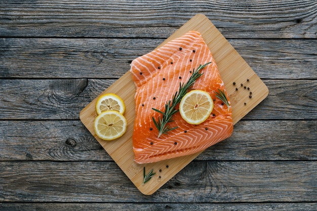 Raw salmon fillet with lemon rosemary and pepper on cutting board fresh organic wild atlantic fish on wooden background mediterranean cuisine healthy and diet food concept