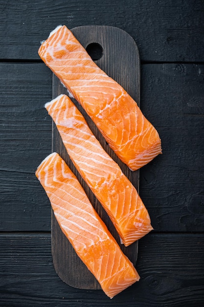 Raw salmon fillets, on black wooden table, top view