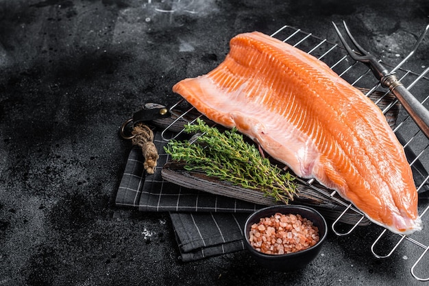 Raw salmon fish fillet cooking steaks on grill with herbs Black background Top view Copy space