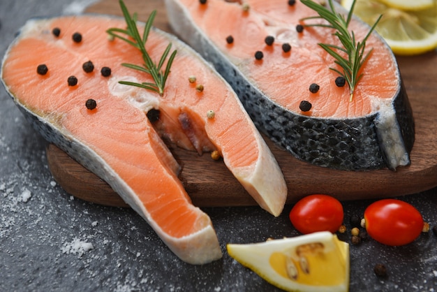 Raw salmon fish fillet and ice for cooked steak seafood - Fresh salmon steak with herbs and spices lemon rosemary tomato on wooden cutting board background