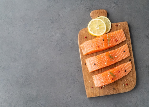 Raw salmon slices with seasonings over wooden board with copy space