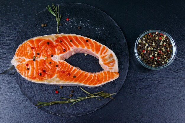 Raw salmon steak with spices on black slate Top view