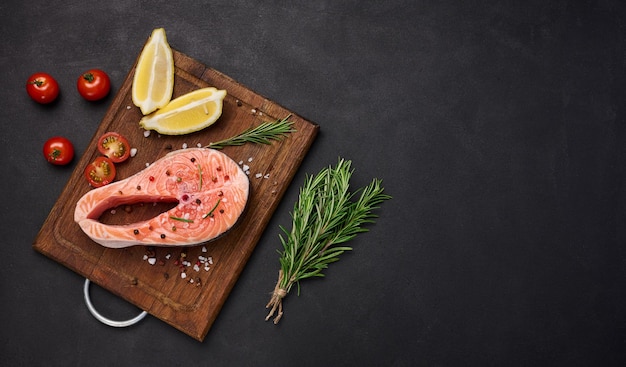 Raw salmon steak on a wooden cutting board lemon slices spices Top view on black table