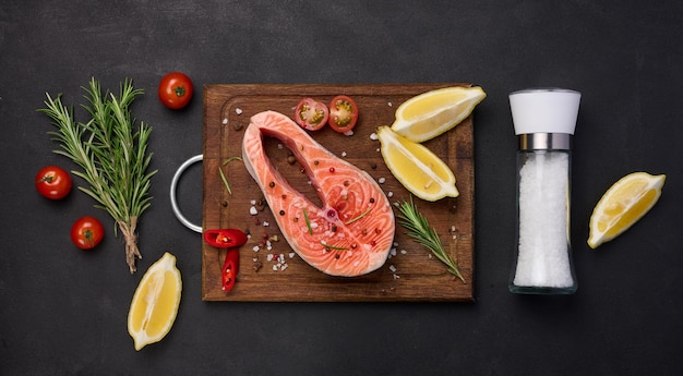 Raw salmon steak on a wooden cutting board lemon slices spices Top view on black table