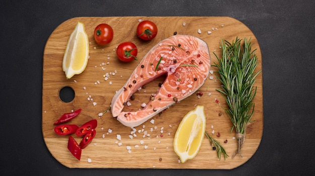 Raw salmon steak on a wooden cutting board lemon slices spices Top view on black table