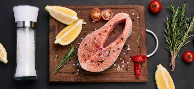 Raw salmon steak on a wooden cutting board lemon slices spices Top view on black table