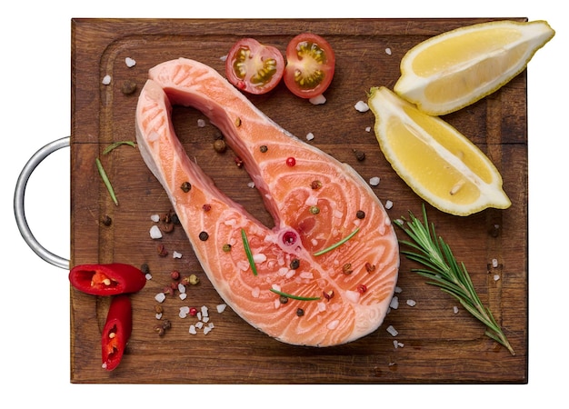 Raw salmon steak on a wooden cutting board lemon slices spices Top view white isolated background