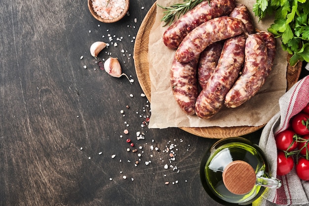 Raw sausages or bratwurst on parchment paper and ingredients for cooking. Top view with copy space on stone table.