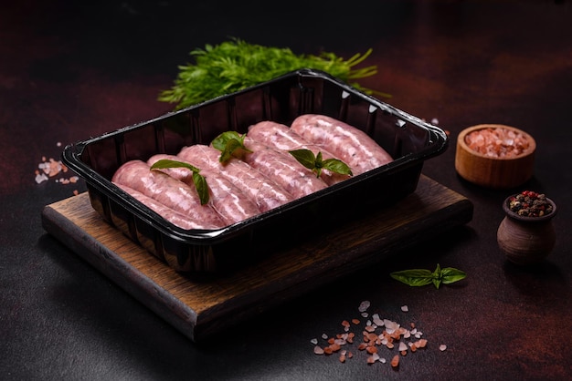 Raw sausages with ingredients on a cutting board on a dark concrete background with copy space