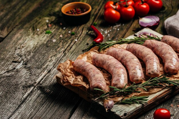 Raw sausages with spices and rosemary on cutting board on light background Cooking ingredients Natural healthy food concept top view