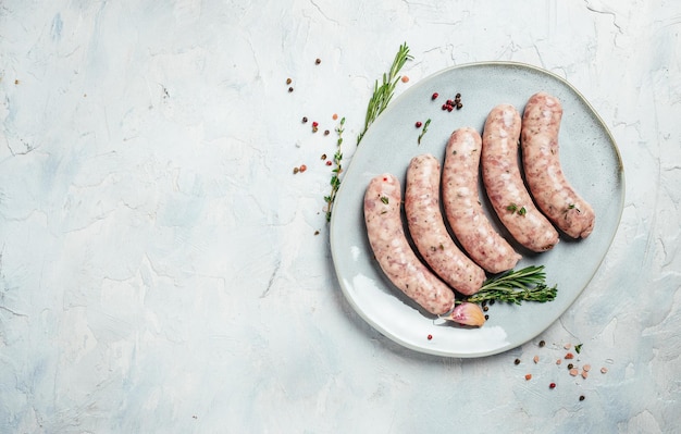 Raw sausages with spices and rosemary on plate on light background Cooking ingredients Natural healthy food concept top view