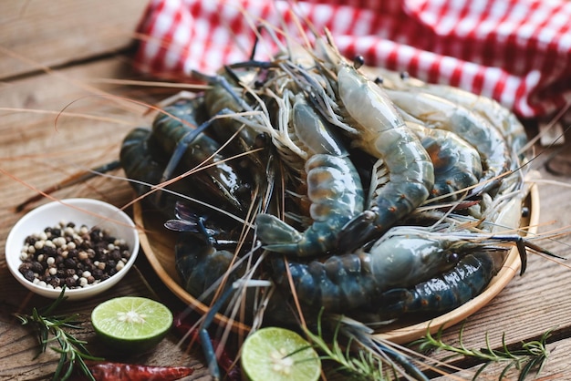 Raw shrimp on plate wooden background for cooking food fresh shrimps prawns seafood shelfish with herb and spices chilli pepper lemon lime rosemary