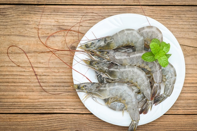 Raw shrimp on white plate with mint leaf and shrimps wooden background for cooking close up fresh shrimps or prawns seafood shelfish top view