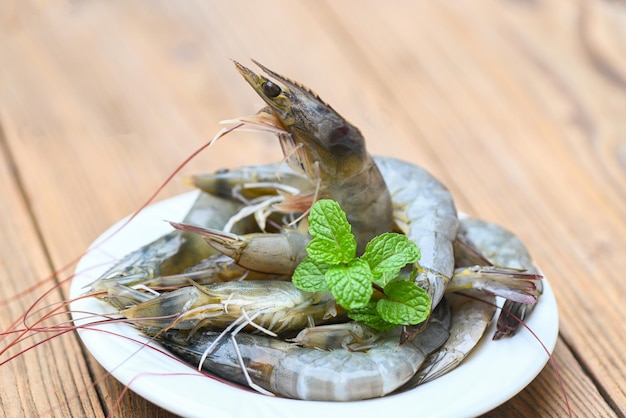 Raw shrimp on white plate with mint leaf and shrimps on wooden background for cooking close up fresh shrimps or prawns seafood shelfish