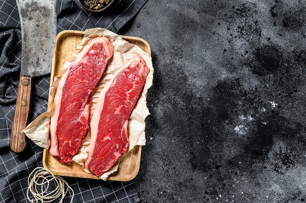 Raw sirloin steak on a wooden tray with a meat cleaver. Marble beef.. Copy space