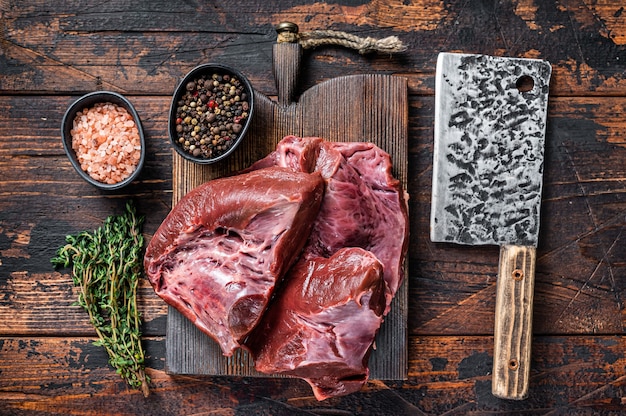 Raw sliced Beef or veal heart on a cutting board with meat cleaver. Dark wooden table. Top View.