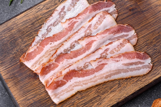 Raw smoked bacon slices on a wooden board with spices and herbs