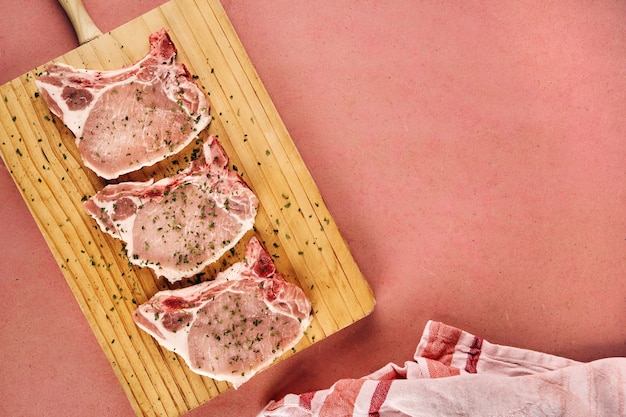 Raw and spiced pork chops on a wooden cutting board and copy space