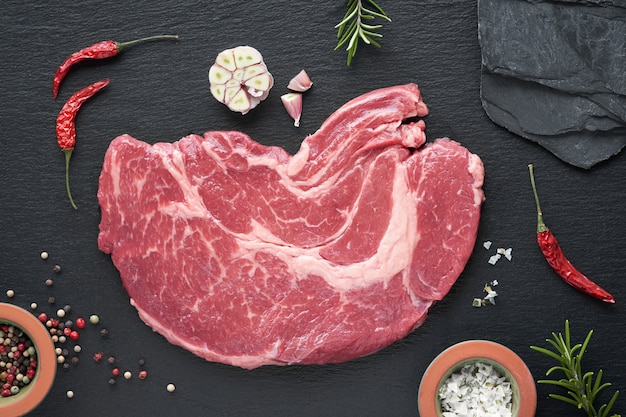 Raw steak. Meat with spices and herbs on black slate stone background, flat lay