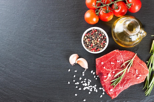 Raw steak with cooking ingridients on black slate background