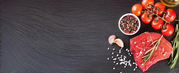 Raw steak with cooking ingridients on black slate background