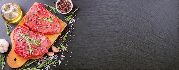 Raw steak with cooking ingridients on black slate background