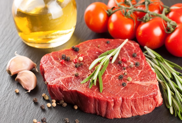 Raw steak with cooking ingridients on black slate background