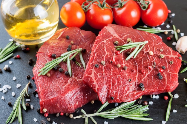 Raw steak with cooking ingridients on black slate background