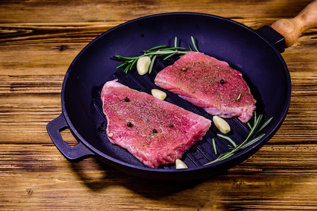 Raw steaks with garlic rosemary and spices in a cast iron grill pan